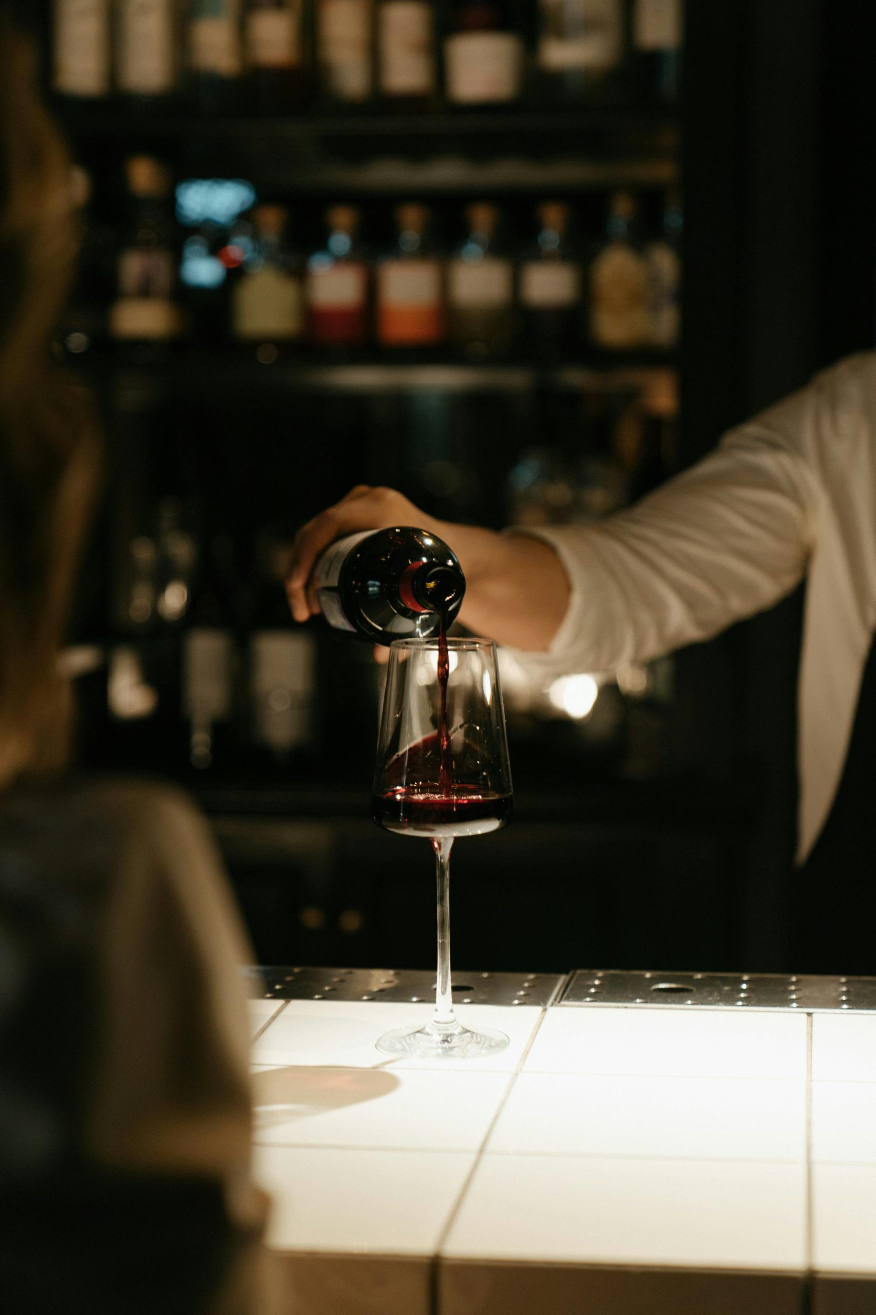 Accueil An elegant scene of red wine being poured at a dimly lit bar counter.