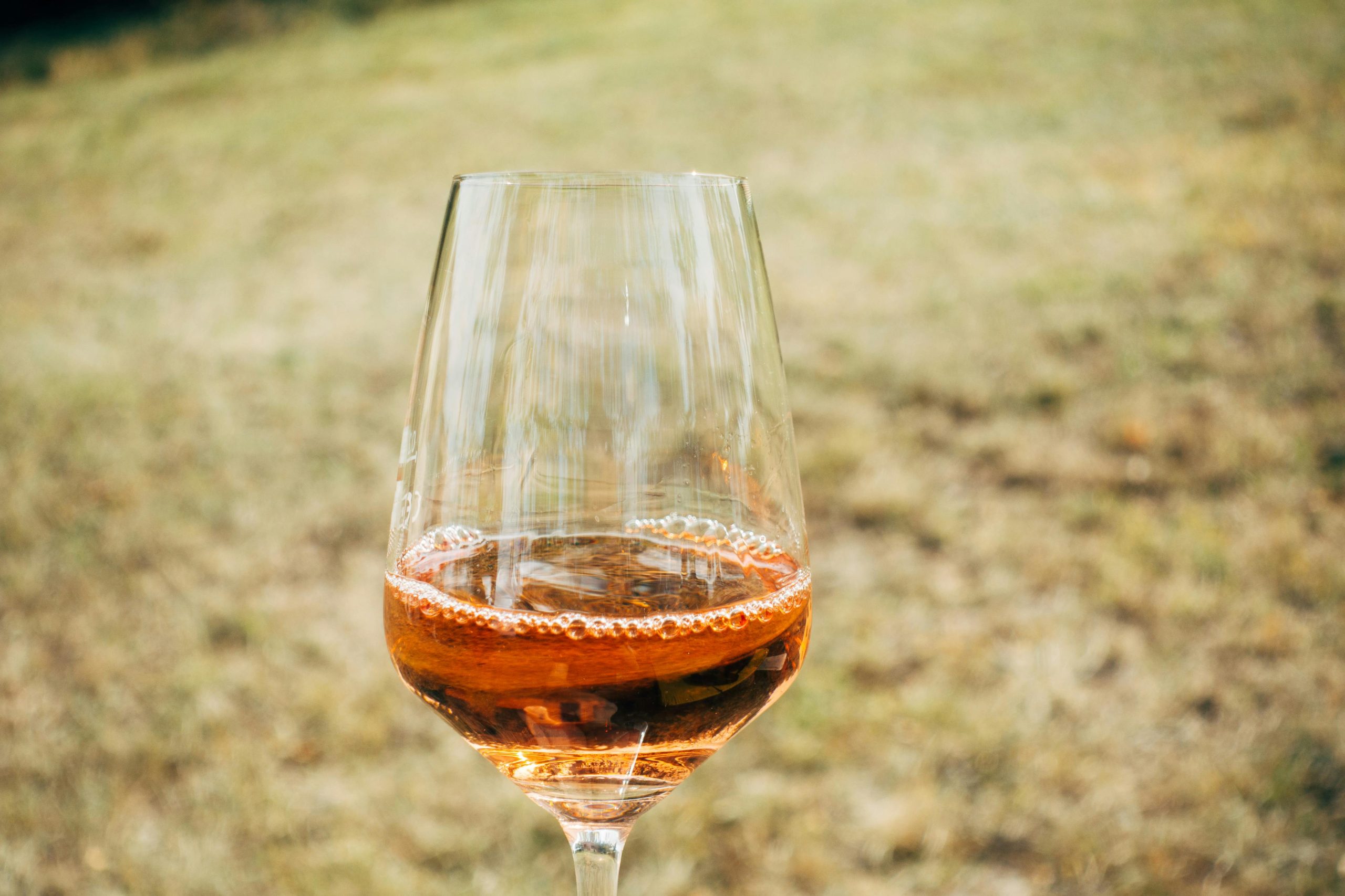 Accueil A sparkling glass of rose wine captured with a blurred outdoor background on a sunny day.