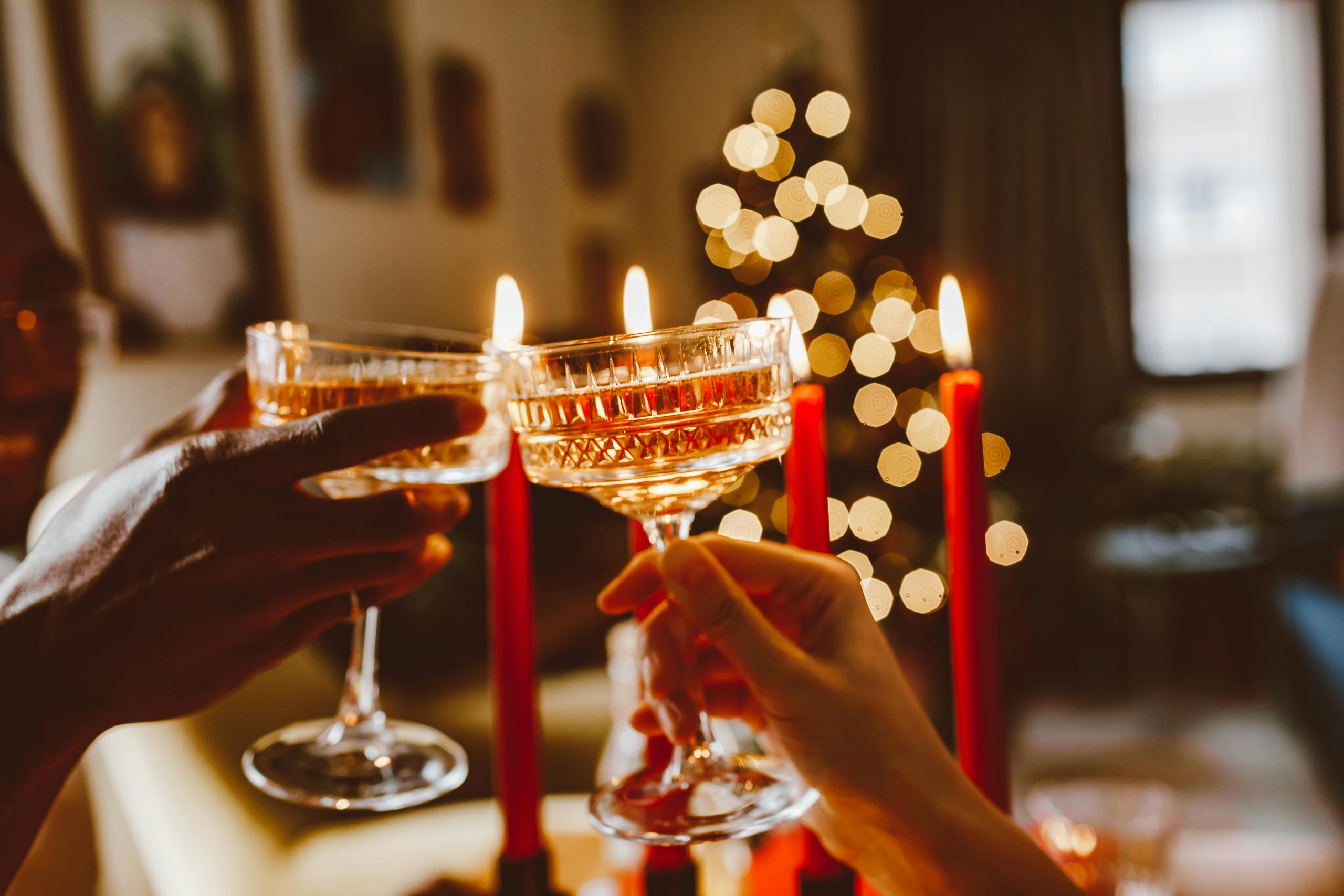 Accueil Two people toast with champagne glasses in a festive, candlelit setting with Christmas decorations.